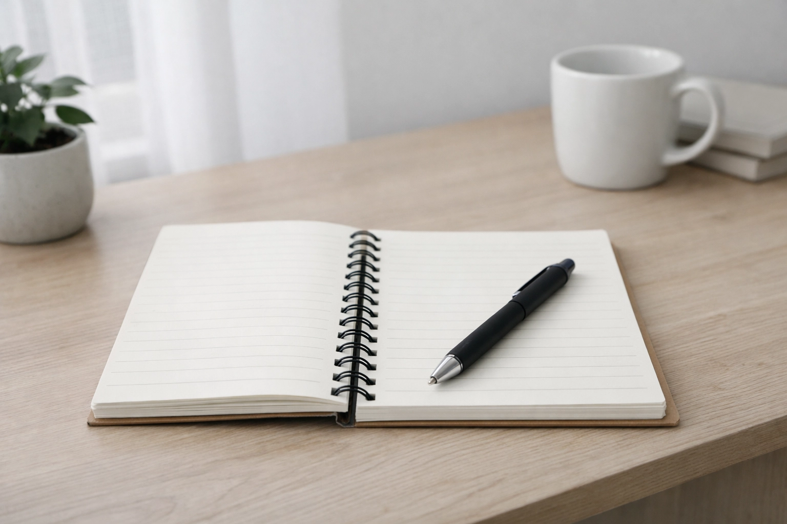 A simple wooden desk with a notebook and pen in soft, neutral daylight.